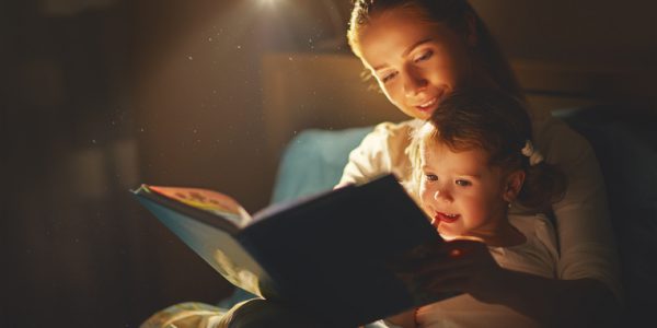 mother and child girl reading a book in bed before going to sleep